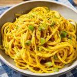 Plate of flavorful garlic noodles garnished with green onions and sesame seeds.