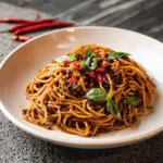 Delicious bowl of Umami Chili Garlic Noodles garnished with herbs.